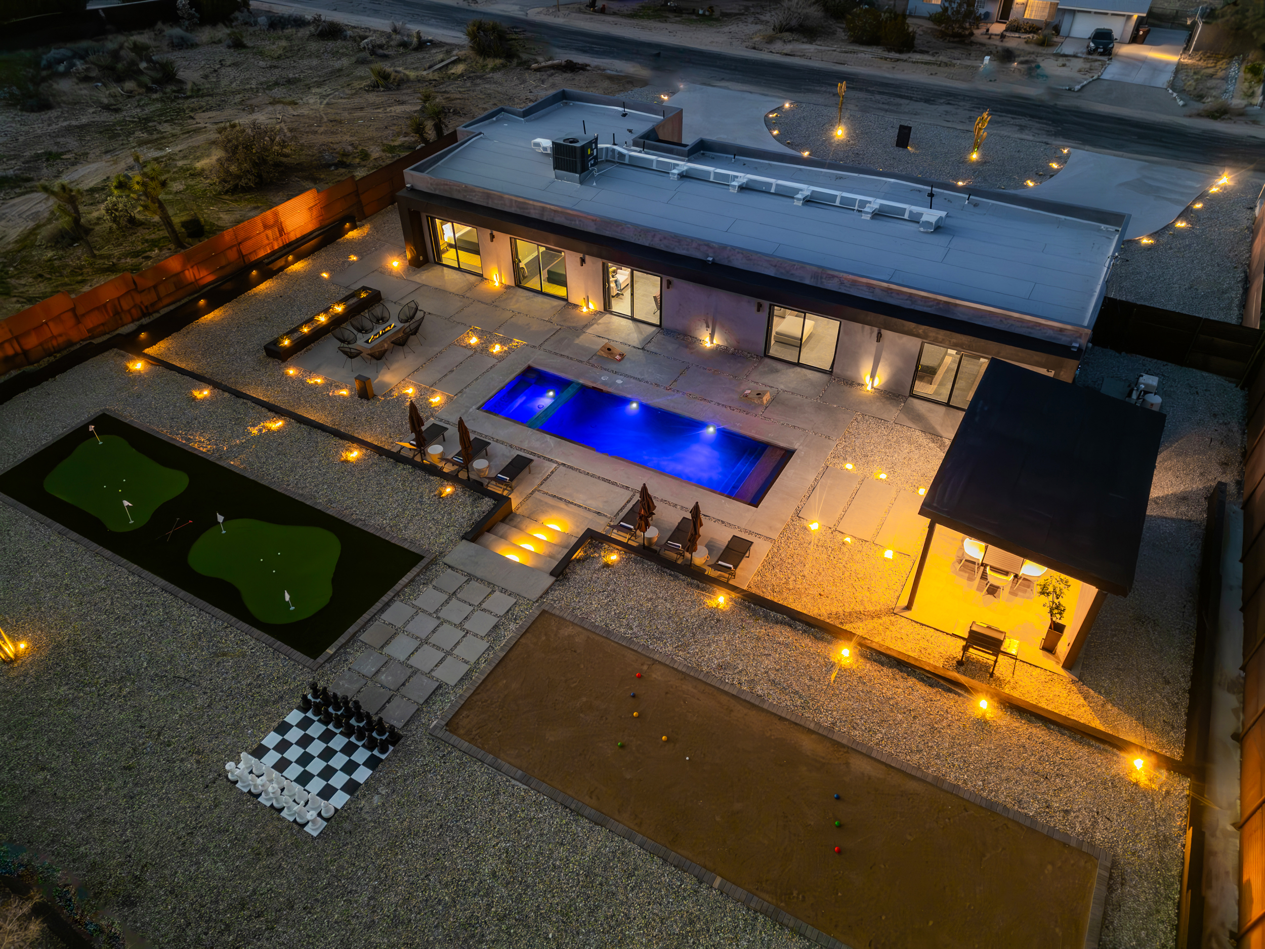 Aerial night view of the backyard putting greens, bocce court, and giant chessboard with mountains beyond